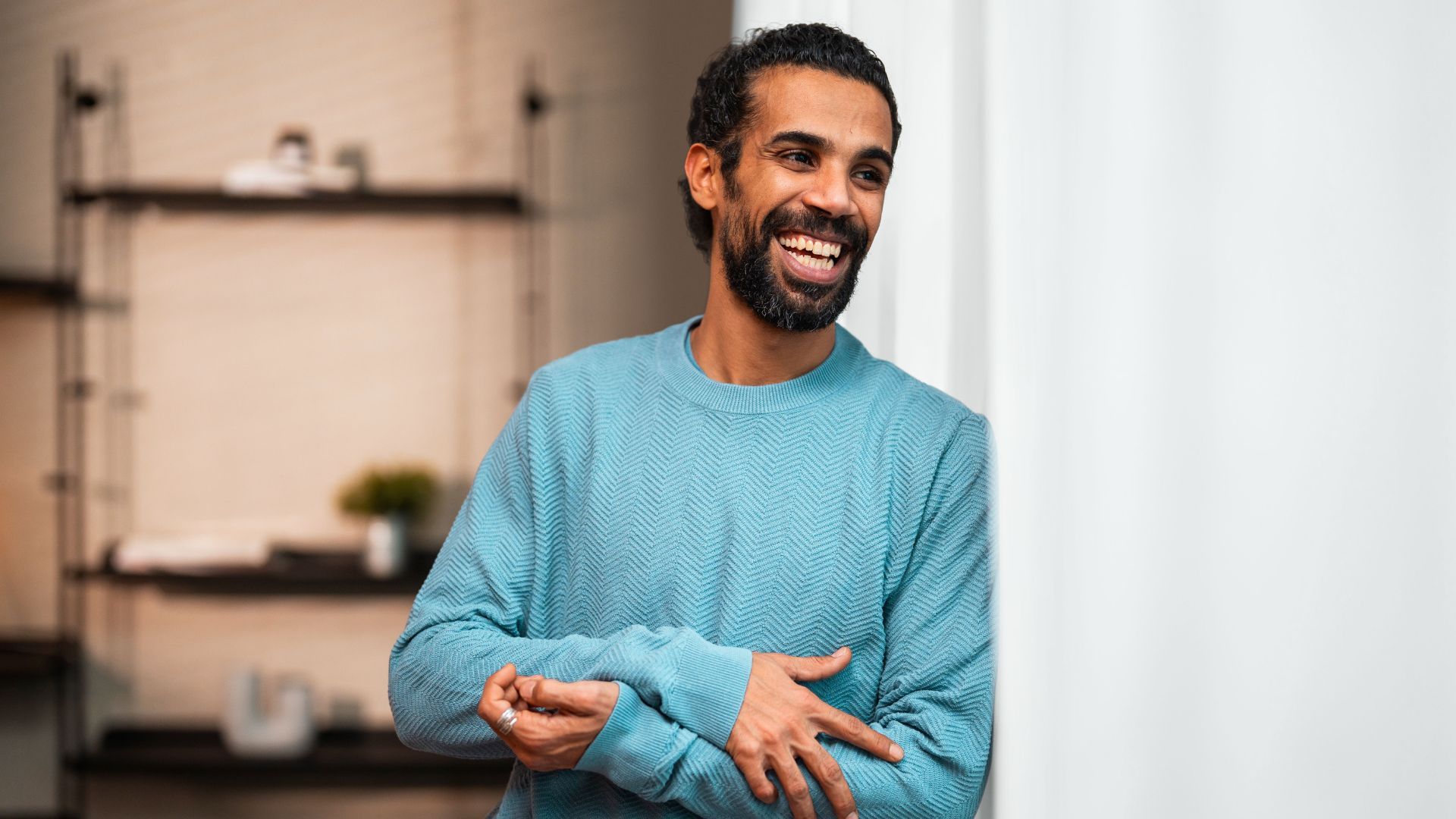 Smiling man in a blue sweater standing indoors.