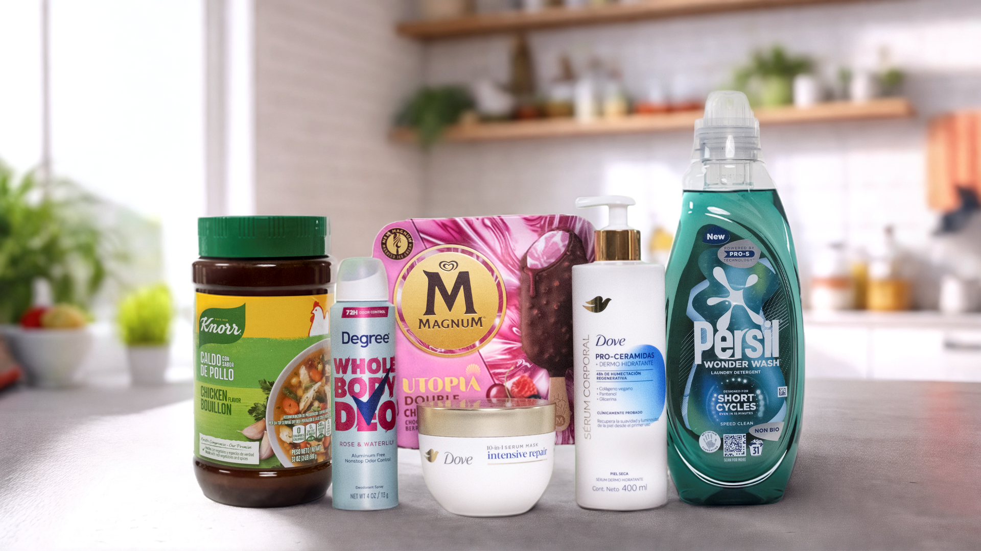 A variety of Unilever's Power Brands arranged on a kitchen counter. From left to right, you can see a jar of Knorr chicken bouillon, a Degree deodorant spray labelled "WHOLE BODY DEO", a box of Magnum ice cream labelled "UTOPIA", a bottle of Dove body lotion pro-ceramides serum, a jar of Dove Intensive Repair cream and a bottle of Persil Wonder Wash. In the background, there's a modern kitchen with plants and various items on the shelves.